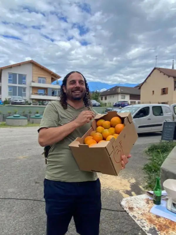 Julien porte une caisse d'oranges cultivées par des producteurs de fruits andalous issus de circuits courts, durables et bio, à retrouver au marché de producteurs en Haute-Savoie