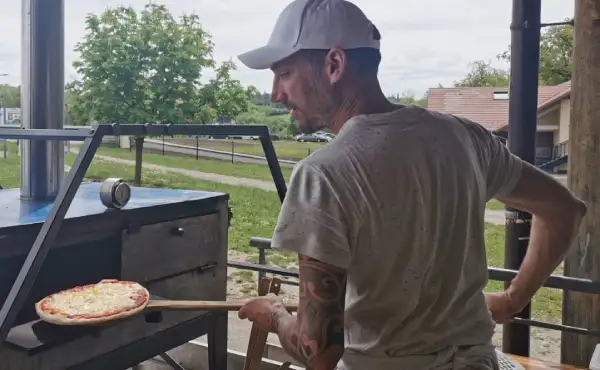 Pizzaiolo et boulanger de Croq'en Pâte en train d'enfourner une pizza au feu de bois, à Savigny en Haute-Savoie